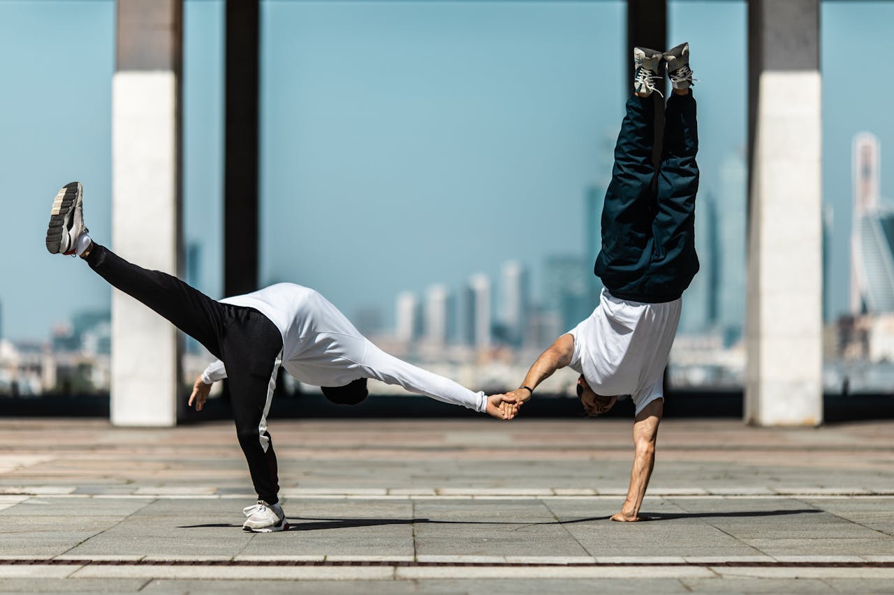 Two dancers perform a dynamic street dance move outdoors, showcasing balance and synchronization.